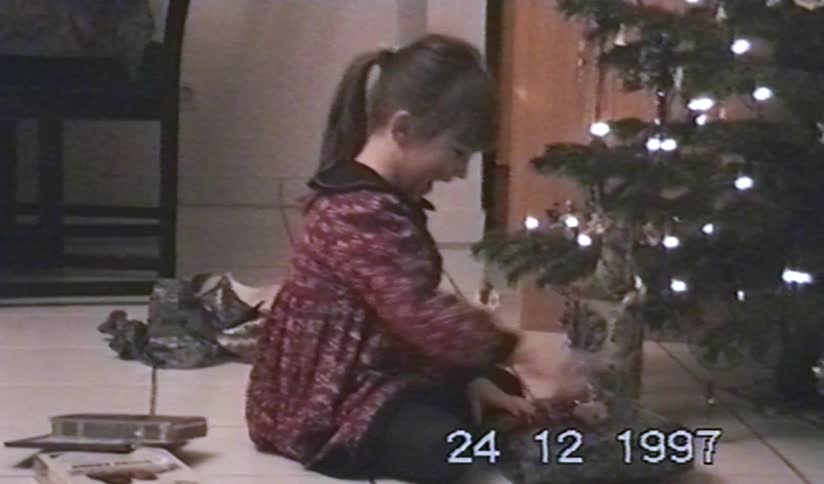 Vintage VHS footage from 1997 shows an excited young girl unwrapping her presents on Christmas Eve next to the tree