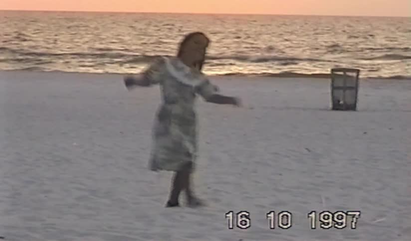Vintage home video from 1997 shows a young girl in a dress dancing joyfully on the beach as the sun sets over the ocean