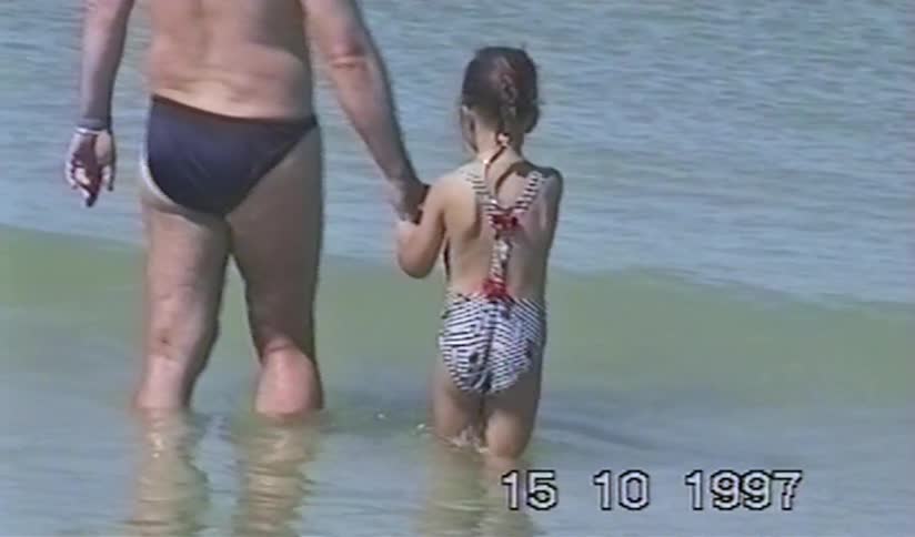 Archival footage from 1997 shows a grandfather and his young granddaughter holding hands in the calm ocean