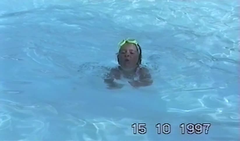 Nostalgic 1997 home video of a father teaching his young daughter to swim in a pool as she laughs and plays in the water