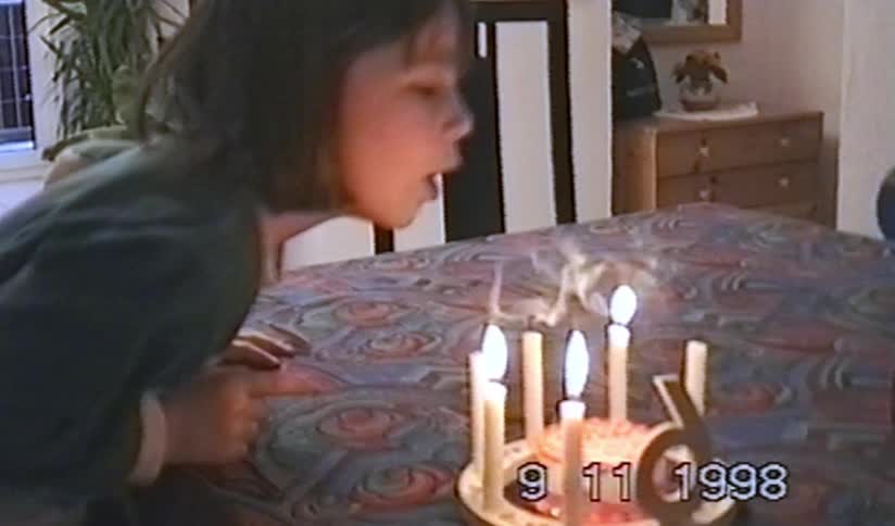 A young girl celebrating her 6th birthday blows out the candles on her cake in a nostalgic home video from 1998