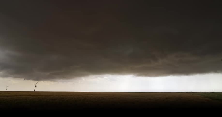 A massive, dark shelf cloud from an approaching thunderstorm ominously rolls over a golden agricultural field
