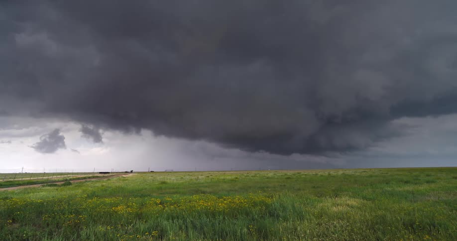 An ominous supercell thunderstorm with dark, churning clouds moves across a vibrant green prairie