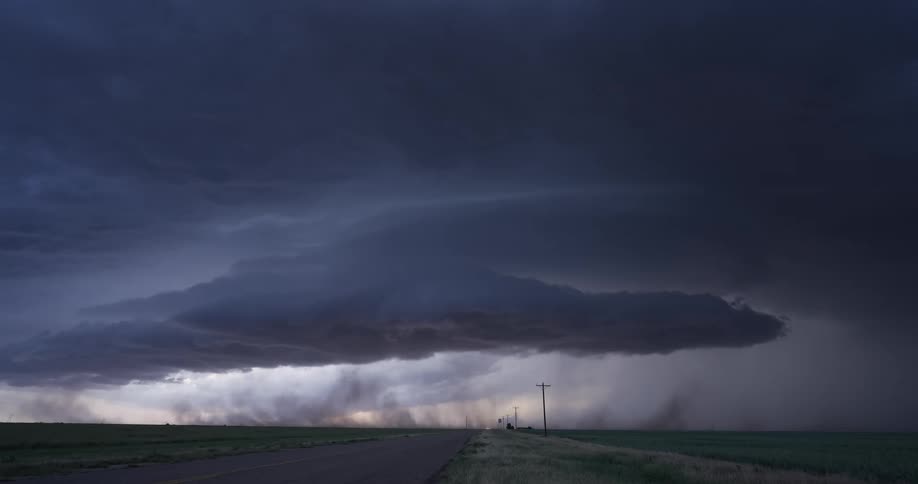 An ominous supercell thunderstorm with a tornado and lightning looms over a lonely country road as a vehicle passes by
