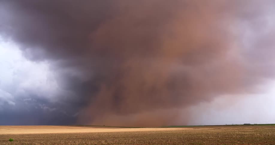 A massive, swirling haboob dust storm moves across a vast, empty field under dark, ominous storm clouds