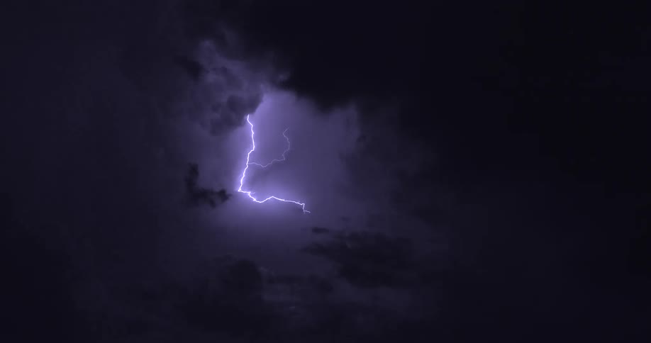Flashes of powerful purple lightning strike through dark clouds during a dramatic nighttime thunderstorm