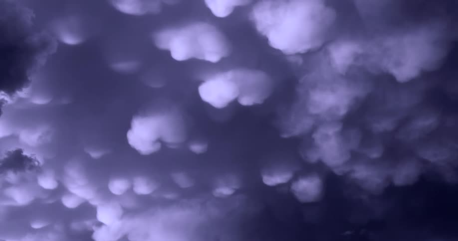 A low-angle view of ominous, dark purple mammatus clouds filling the stormy sky