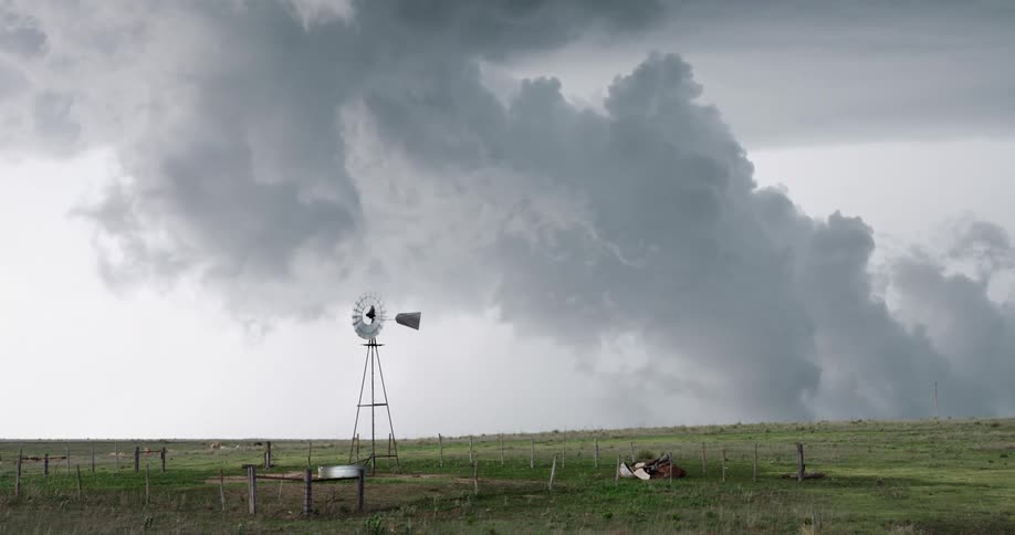 A windmill stands still in a wide-open field under massive, dark, and foreboding storm clouds
