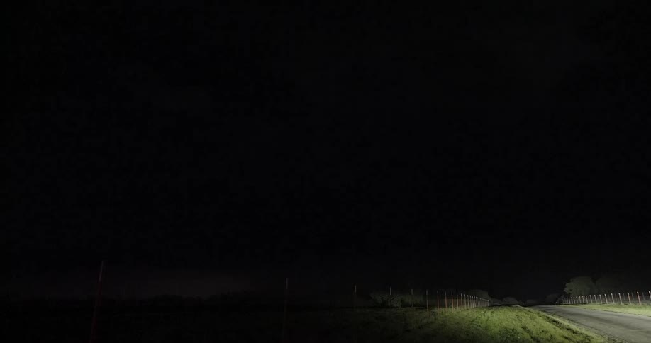 A powerful thunderstorm with frequent lightning illuminates the night sky over a rural road