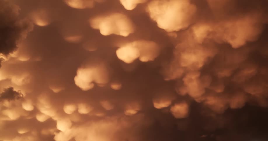 A dreamy, soft-focus view of rare orange Mammatus clouds hanging in a stormy sky at sunset