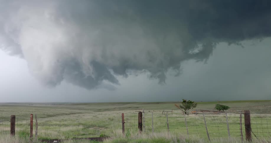 A massive supercell thunderstorm with ominous, rotating clouds hangs over a vast rural landscape