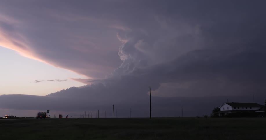 A dramatic time-lapse captures a powerful supercell thunderstorm forming over a rural highway at sunset