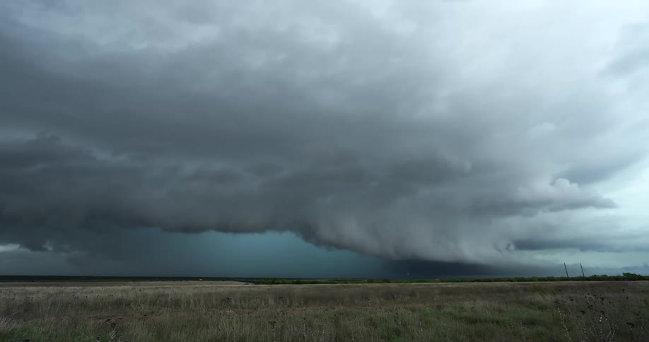 An ominous and powerful shelf cloud from a supercell thunderstorm looms over a rural landscape