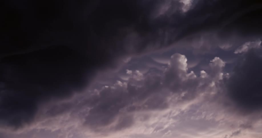 Dark purple and grey storm clouds slowly move across a dramatic evening sky