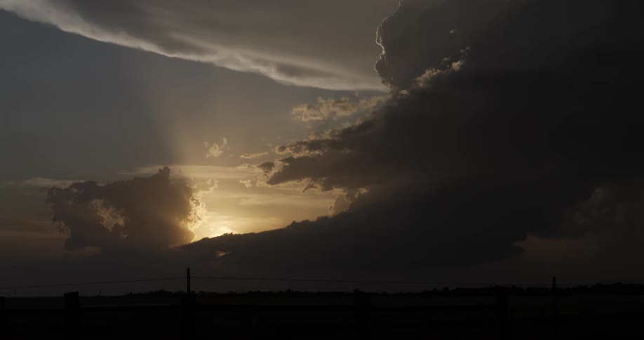 Dramatic storm clouds drift across the sky as golden sun rays shine through during a beautiful sunset