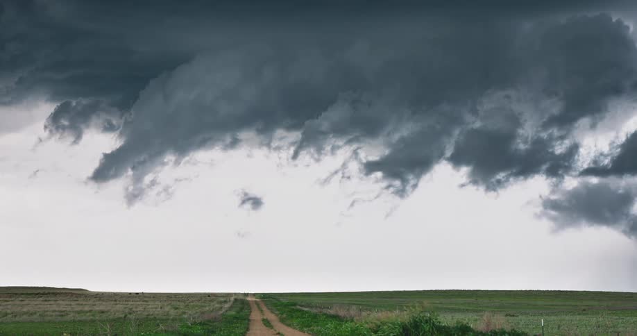 An ominous shelf cloud from an approaching severe thunderstorm moves over a dirt road in the countryside