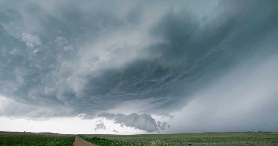 A dramatic wide shot of a massive supercell thunderstorm with ominous clouds churning over a rural plain and a dirt road