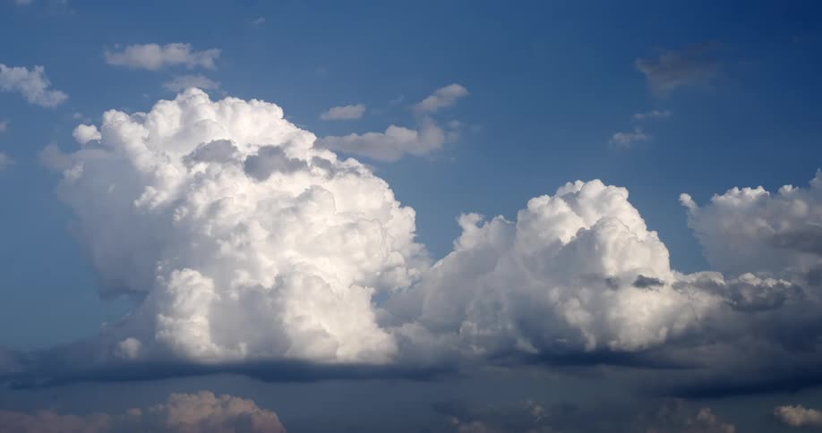 Dramatic white cumulus clouds float serenely in a bright blue sky