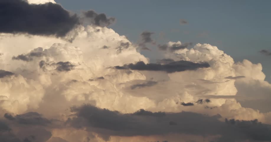 Dramatic golden hour light illuminates a massive formation of puffy white and dark storm clouds in the sky