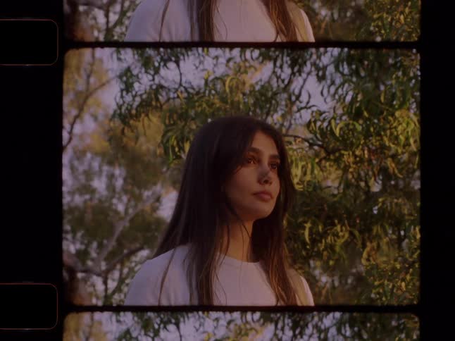 Vintage 16mm multi-frame film shows a young woman walking down a country road and posing thoughtfully in a forest at golden hour