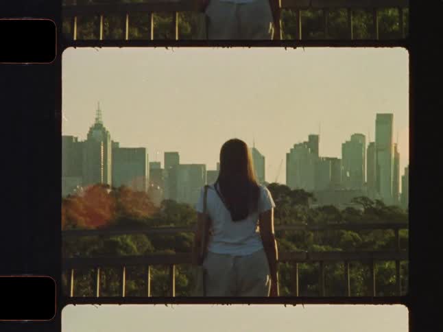Vintage film captures a young woman looking out at a beautiful city skyline during a warm golden hour sunset