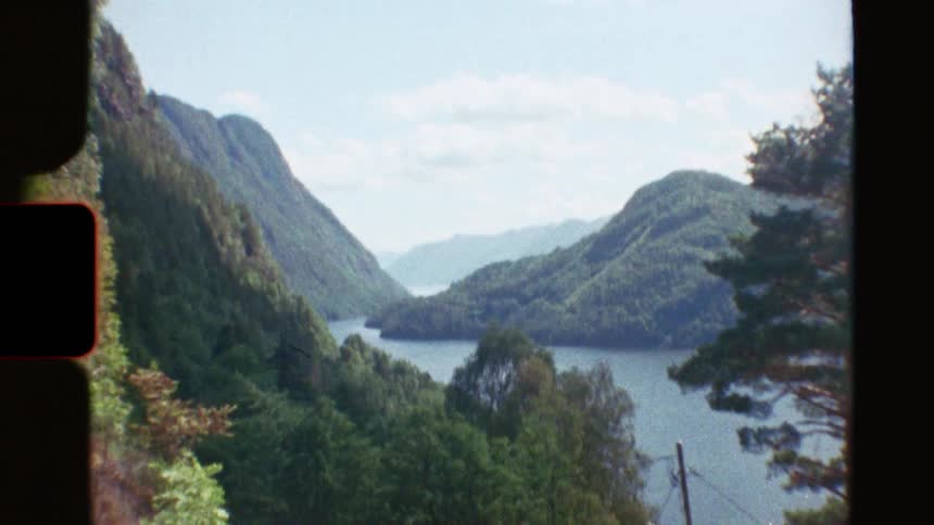 Super 8mm footage shows a car driving on a scenic road before tilting up to a stunning view of a Norwegian fjord