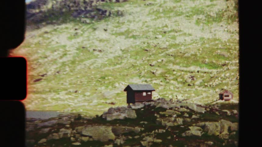 Vintage Super 8 film of a small, isolated cabin in a rugged, green mountain landscape