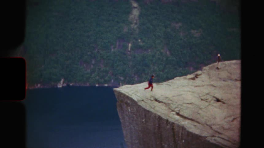 Vintage footage shows a hiker sitting on the edge of a massive cliff before standing up and walking away from the precipice
