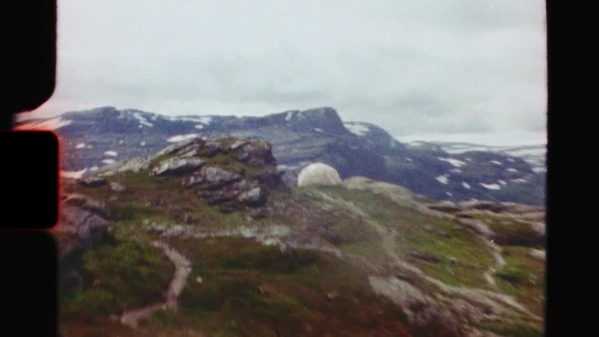 Shaky handheld vintage footage reveals a remote, snow-capped mountain range with a dome observatory