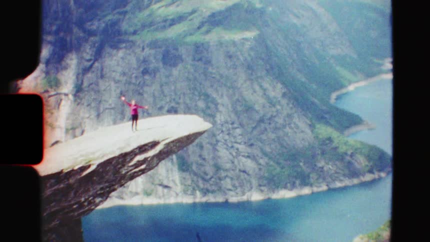 Authentic 8mm film captures a hiker walking to the edge of the dramatic Trolltunga cliff in Norway and raising their arms in triumph