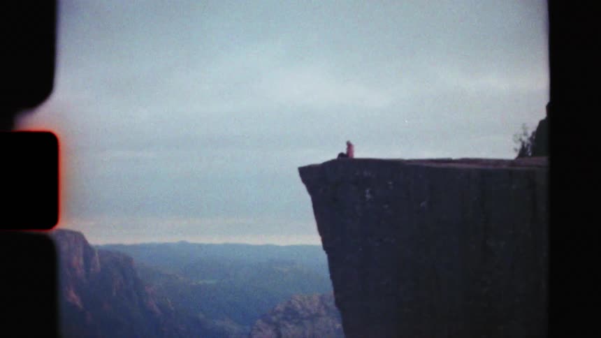 Vintage super 8mm film reveals a lone person sitting on the edge of a massive cliff overlooking a stunning Norwegian fjord