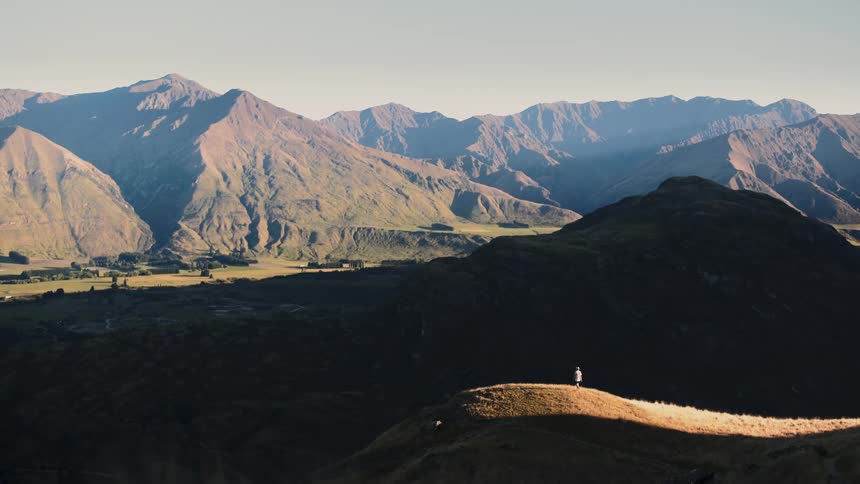 A lone adventurer hikes to a sun-drenched ridge to admire the magnificent mountain valley at sunrise