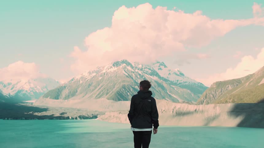 A solo traveler in a black jacket takes in the spectacular view of a turquoise glacial lake and snow-capped mountains