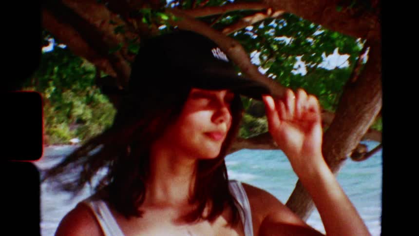 A woman in a cap enjoys a breezy day on a tropical beach in this dreamy, vintage-style footage