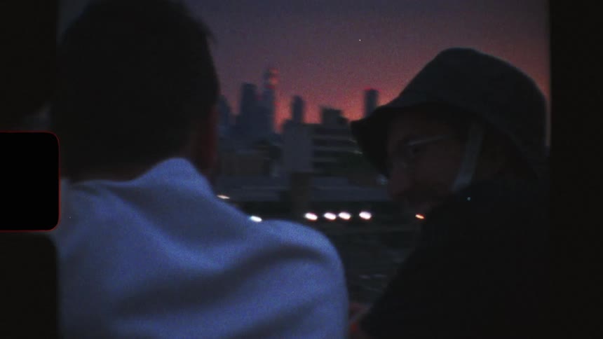 Vintage 8mm footage captures two people watching a train pass by the London skyline at dusk