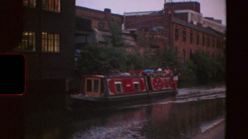 Vintage super 8 footage shows two men jogging along an urban canal path before panning to a red narrowboat cruising by