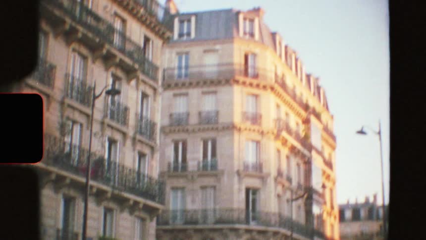 An authentic Super 8 film captures a romantic Parisian cafe at dusk before tilting up to reveal a classic sun-kissed building