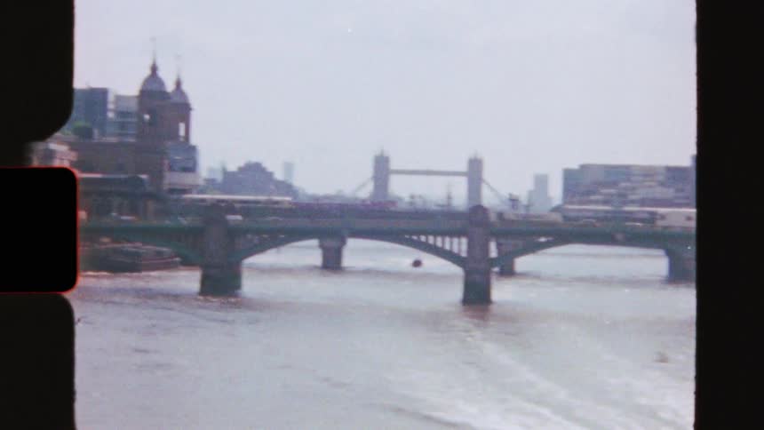 Vintage 8mm footage captures a speedboat cruising down the River Thames, revealing the iconic Tower Bridge in the London city skyline