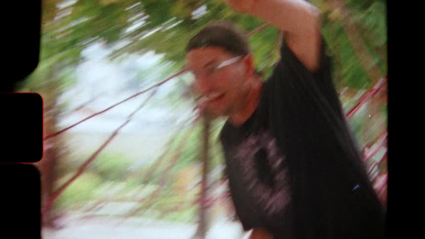 Super 8 footage shows a man with a backwards cap laughing while playing table tennis in a park