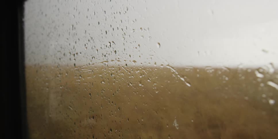 Water droplets on a vehicle's window as it drives through a field