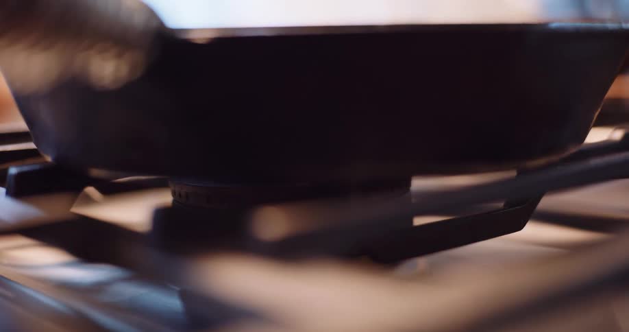 A cast iron skillet heats up over the blue flame of a gas stove burner in a close-up shot