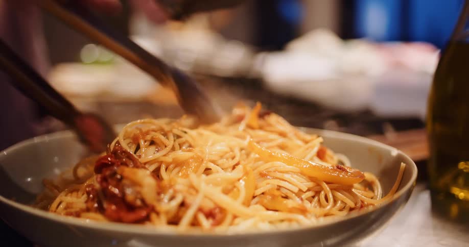 A chef plates a delicious, steaming hot bowl of spaghetti with a savory sauce in a beautiful slow-motion close-up