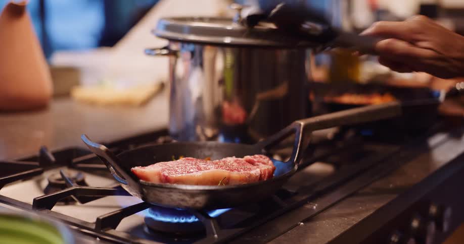 A close-up slow-motion shot of a juicy steak being seared in a hot skillet on a gas stove