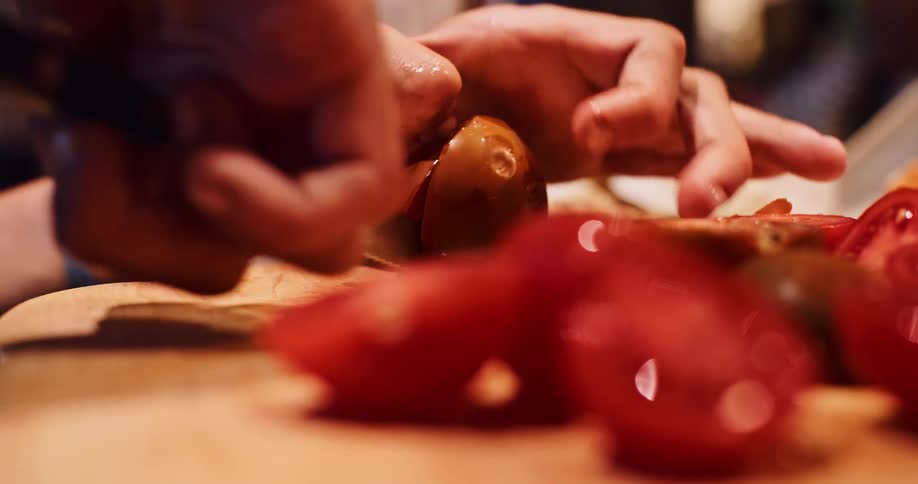 An extreme close-up shot of a person's hands carefully slicing a ripe tomato on a wooden cutting board