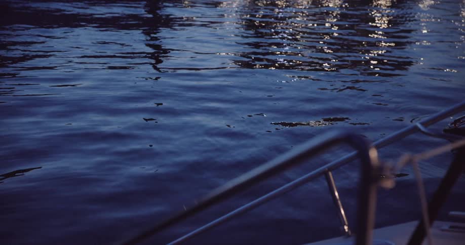 Shimmering light reflects on dark blue water from the bow of a boat at night