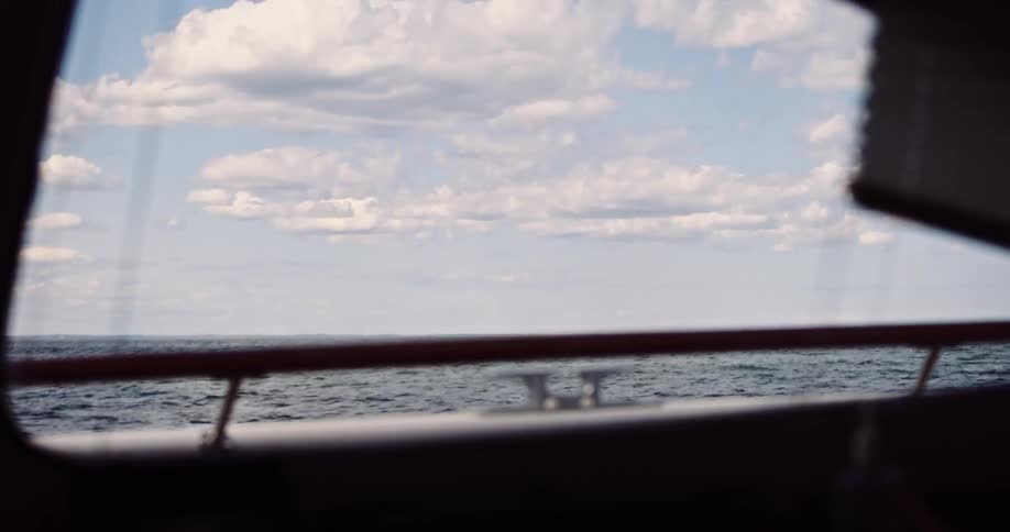 A view of the ocean and cloudy sky from the window of a moving boat, with a person briefly entering the frame
