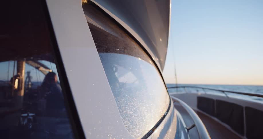 Golden hour sunlight shines on the salt-sprayed windshield of a luxury yacht cruising on the open ocean