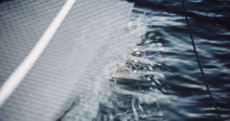 The hull of a modern sailboat slices through the ocean waves in dramatic slow motion