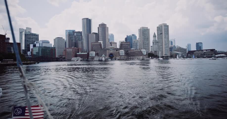 A slow-motion view from a moving boat showing the Boston city skyline from the water on a cloudy day