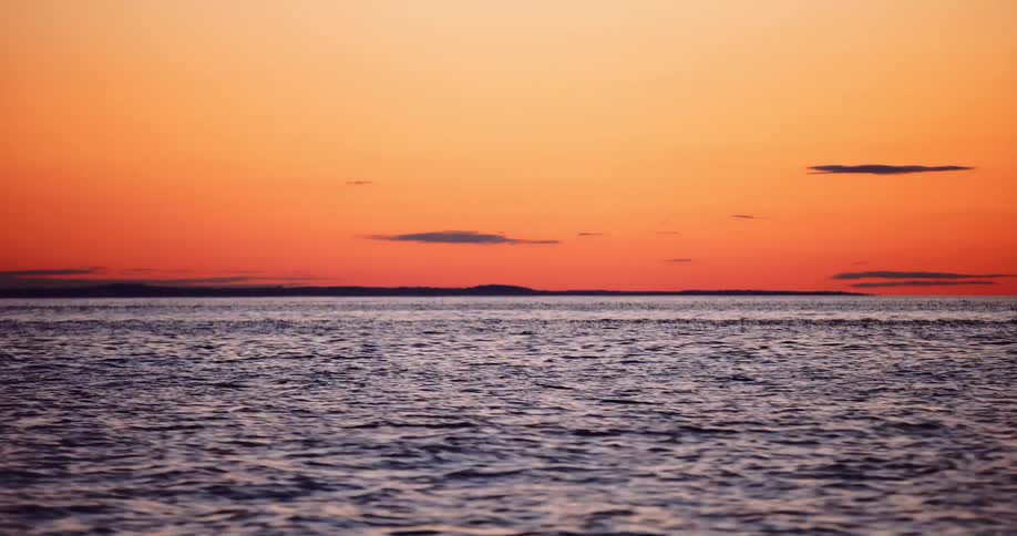Gentle ocean waves ripple under a stunning orange and red sky at sunset